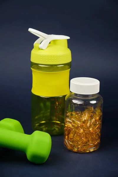Agitador de plástico, pesas verdes y una lata de omega 3 sobre un fondo azul —  Fotos de Stock
