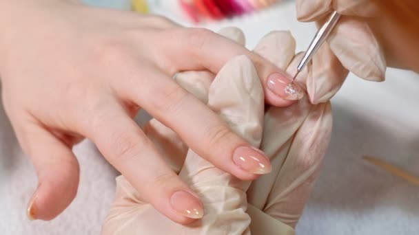 El maestro de la manicura aplica un esmalte de uñas brillante a las uñas de los clientes en un salón de belleza. dibujar un corazón en las uñas de los clientes. De cerca. . — Vídeo de stock