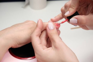 Manikür ustası bir güzellik salonundaki müşterinin tırnaklarına parlak bir oje sürüyor. Müşterinin tırnaklarına kalp çizmek. Kapat..