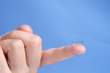 Mavi arka planda parmak ucundaki kontakt lensler,