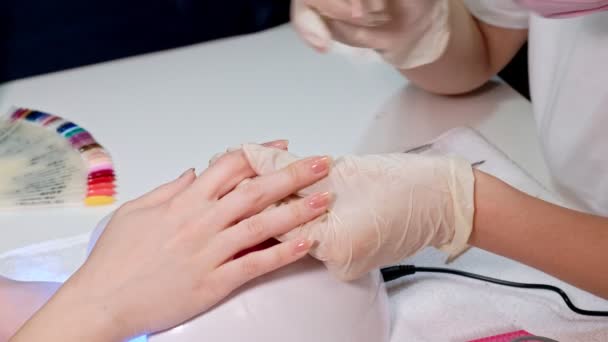 Manikyrmästaren applicerar Nude nail Polish på klientnaglarna i en skönhetssalong. Närbild. — Stockvideo