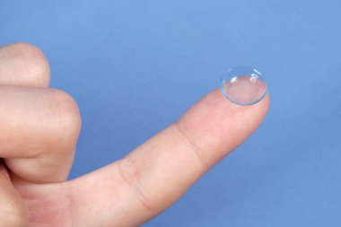 Mavi arka planda parmak ucundaki kontakt lensler,