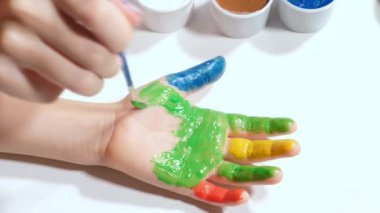 Küçük bir kız renkli parmaklarıyla beyaz bir kağıda resim çiziyor.