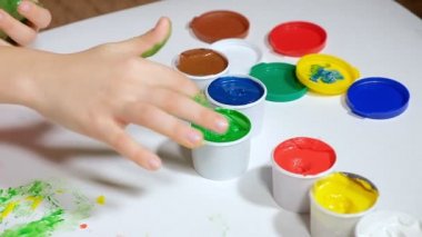 Küçük bir kız renkli parmaklarıyla beyaz bir kağıda resim çiziyor.