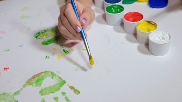 Uma menina desenha com pinturas coloridas em um papel branco — Vídeo de Stock