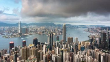 Hong Kong şehrinin yüksek dağdaki Victoria tepesinden gece gündüz görüntüsü günbatımında Hong Kong şehrinde günbatımında gökdelenler, gökdelenler ve tekne taşımacılığı ve birçok modern apartmanla birlikte seyahat için ünlü bir dönüm noktasıdır.