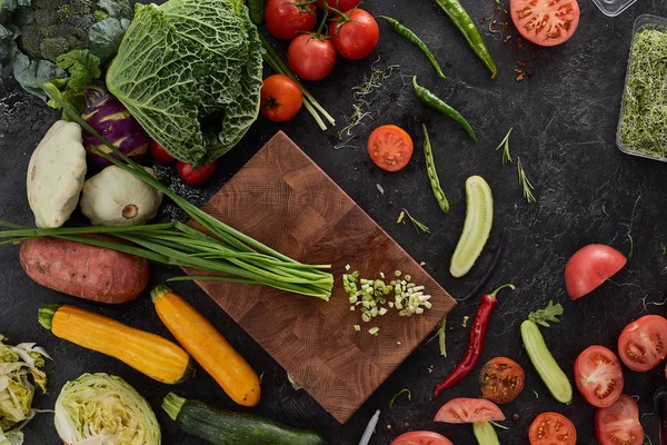 Taze organik yeşil soğan sebze kesme tahtası üzerinde siyah taş Resepsiyon arka plan üzerinde. Sağlıklı doğal gıda rustik ahşap üzerine. Domates, marul, havuç, biber, kabak ve diğer malzemeler üstten görünüm pişirme