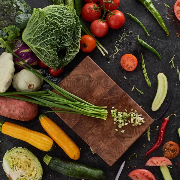 Taze organik yeşil soğan sebze kesme tahtası üzerinde siyah taş Resepsiyon arka plan üzerinde. Sağlıklı doğal gıda rustik ahşap üzerine. Domates, marul, havuç, biber, kabak ve diğer malzemeler üstten görünüm pişirme