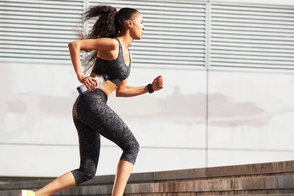 Αθλητική γυναίκα τρέχει μέχρι τα πέτρινα σκαλοπάτια με μπουκάλι νερό στην πόλη με το fitness tracker — Φωτογραφία Αρχείου