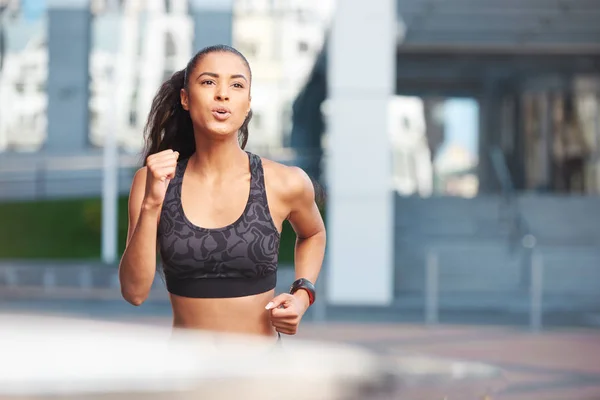 Atletisk kvinna porträtt med allvarliga ansikte körs på gatan i staden framför byggnaden med fitness tracker — Stockfoto