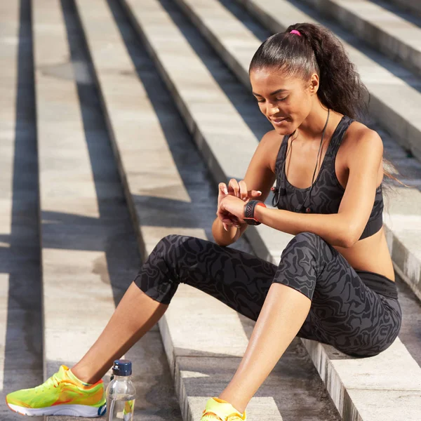 Woman athlete smiling portrait using activity tracker or heart rate monitor after run on the stairs. Outdoor fitness concept. Toned image Stock Picture