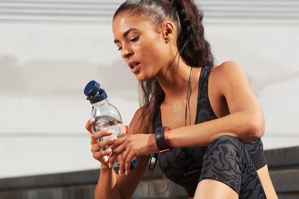 После тяжелой тренировки спортсменка, жаждущая фитнеса, сидит на бутылке. — стоковое фото