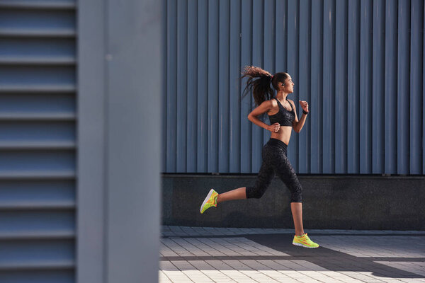 Side view of sporty young woman athlete running on urban street in morning. Health conscious  lifestyle concept with copy space.