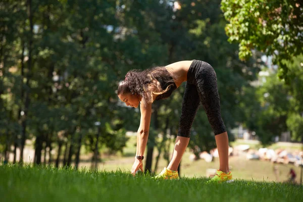 Mujer joven estirándose antes de la sesión de entrenamiento físico en el parque. Una joven saludable calentándose al aire libre. Ella está estirando los brazos y mirando hacia otro lado, hi key . — Foto de Stock