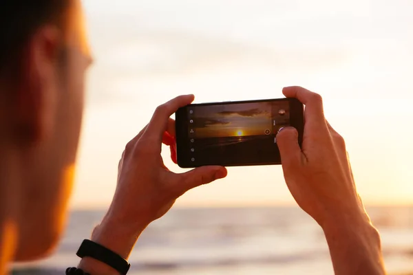 Hücre teknolojisi ve tatil. Erkek el kamerasında akıllı telefon, deniz günbatımının fotoğrafını çekiyor..