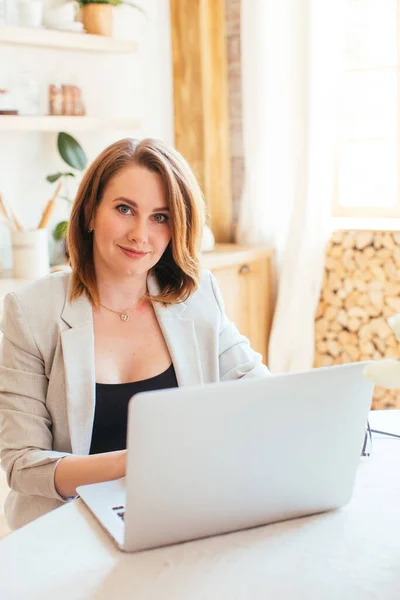 Genç ve güzel bir kadın, mutfaktaki dizüstü bilgisayarı olan bir evden bilgisayar için çalışıyor.