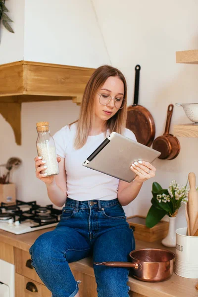 Πορτρέτο μιας ξανθιάς γυναίκας χρησιμοποιώντας έναν υπολογιστή tablet για να μαγειρέψουν στην κουζίνα της — Φωτογραφία Αρχείου