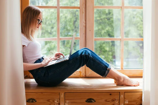 Genç kız öğrenci evde dizüstü bilgisayarıyla çalışıyor. Pencere pervazında evden ders çalışıyorum.