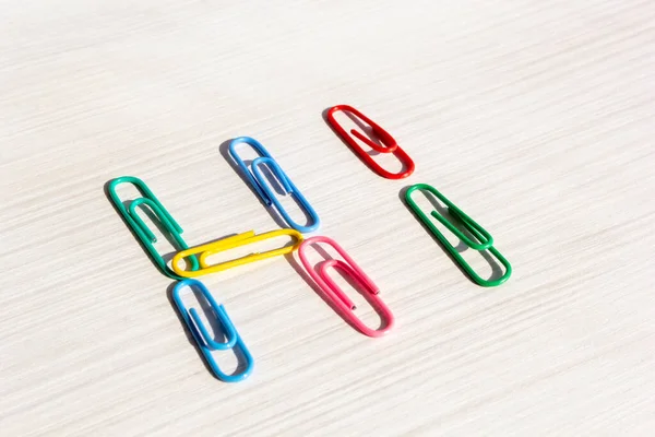 Multicolored paper clips. Paper clip word hello on a light table. Word hello close up. Office and documents concept. Horizontal format