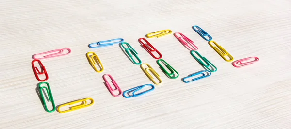 Multicolored paper clips. Paper clip word cool on a light table. Word cool close up. Office and documents concept. Horizontal format