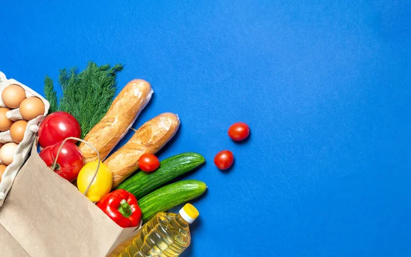 Paper bag with food supplies crisis food stock for quarantine isolation period on blue.Vegetables, oil,egg, herbs, bread isolated. Quarantine, coronavirus, food delivery, Donation.Copy space.Top view.