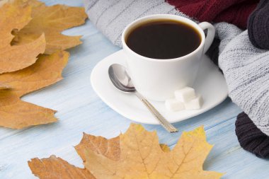 Kahve fincanı, kazak ve sonbahar yaprakları. Mavi ahşap arka planda