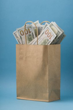 Mavi arka planda içi banknotlarla dolu kağıt çanta. dikey 