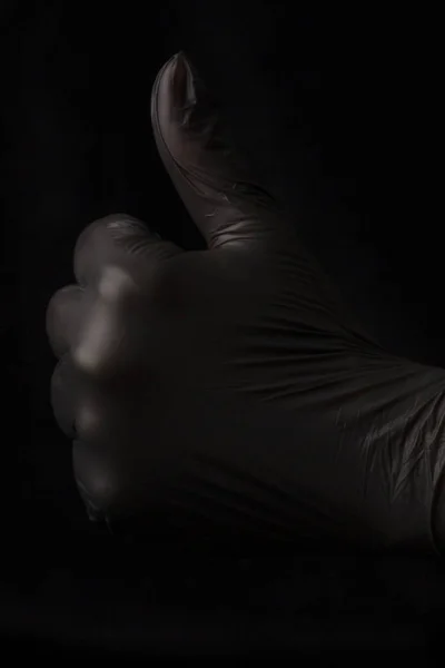 Un brazo con la mano y un guante negro sostiene el pulgar en un —  Fotos de Stock
