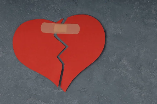 Broken heart shape with bandage on concrete background