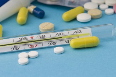 Thermometer and  various tablets on a blue background. 