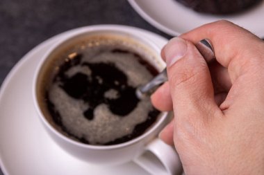 Cup of espresso coffee with hand on dark background
