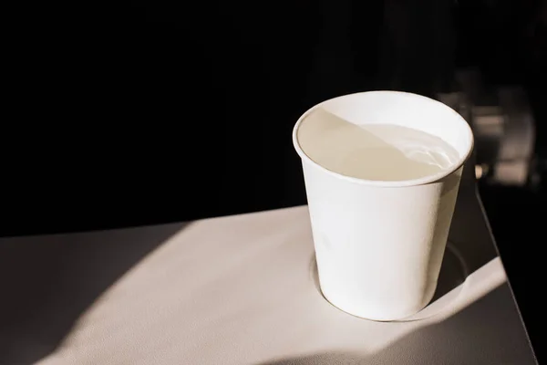 White paper cup of water and headphones on a folding table in an airplane. Drinks on the plane. Dehydration in flight. skin hydration