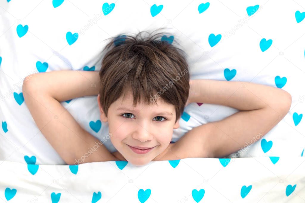 smiling boy in bed. bedding with hearts. emotions. happy morning