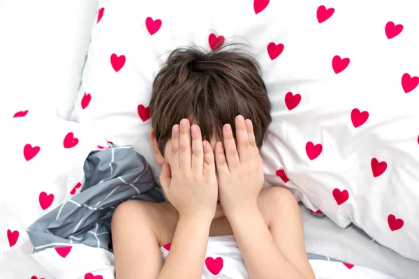 Der Junge liegt in einem Bett mit roten Herzen, das Gesicht in den Händen. Emotionen ohne Gesicht. weiße Farbe, Ansicht von oben — Stockfoto