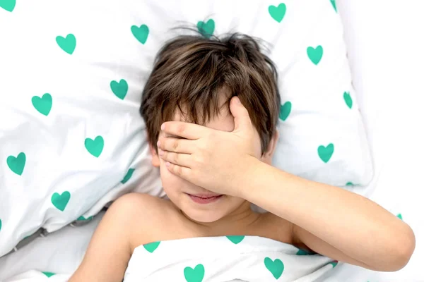 Der Junge liegt in einem Bett mit grünen Herzen, das Gesicht in den Händen. Emotionen ohne Gesicht. weiße Farbe, Ansicht von oben — Stockfoto