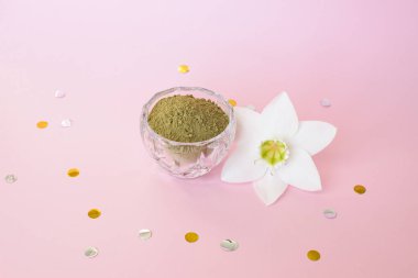 natural henna powder and white flower in a female hand on a pink background. Concept female beauty and cosmetology. Eyebrow and hair coloring.