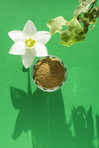 natural henna powder, white flower and plant loach on a green background, vertical. Concept female beauty and cosmetology. Eyebrow and hair coloring.