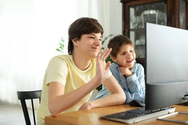Gülümseyen çocuk ve ergen internette sohbet ediyor ve bilgisayar ekranına el sallıyorlar. Koronavirüs yüzünden karantina ve kendini izole etme. COVID-19