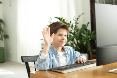 Gülümseyen çocuk ve ergen internette sohbet ediyor ve bilgisayar ekranına el sallıyorlar. Koronavirüsteki karantina sırasında uzaktan öğrenme. Oğlan ve dizüstü bilgisayar evde. Yaşam tarzı. COVID-19