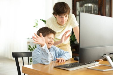 Gülümseyen çocuk ve ergen internette sohbet ediyor ve bilgisayar ekranına el sallıyorlar. Koronavirüs yüzünden karantina ve kendini izole etme. COVID-19