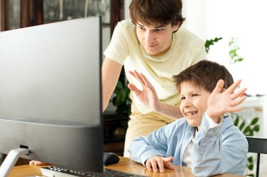 Gülümseyen çocuk ve ergen internette sohbet ediyor ve bilgisayar ekranına el sallıyorlar. Koronavirüs yüzünden karantina ve kendini izole etme. COVID-19