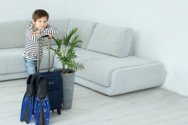 Elinde bavul ve palet olan turist çocuk koronavirüs salgını sırasında evde kalıyor. İzinlerin iptali ve ülkeler arasındaki sınırların kapatılması. Uçuş iptali.