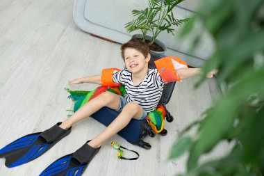 Elinde bavul ve palet olan turist çocuk koronavirüs salgını sırasında evde kalıyor. İzinlerin iptali ve ülkeler arasındaki sınırların kapatılması. Uçuş iptali.