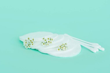 Kulaklar için baton ve pamuk tomurcukları ve küçük beyaz çiçekli turkuaz arka planda pamuktan yapılmış makyaj çıkarıcı..