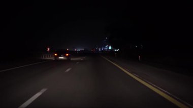 Gece otobanında araba kullanmak, bakış açısı. Şehrin ışıkları görünüyor.
