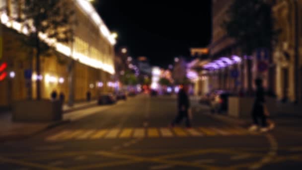 Ослабленный вид на ночную улицу города. Машины едут по дороге. Люди ходят — стоковое видео
