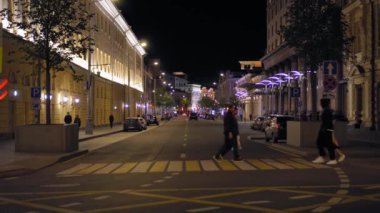 Gece şehir caddesinin odağından çıkmış görüntüsü. Arabalar yol boyunca gider. İnsanlar yürür