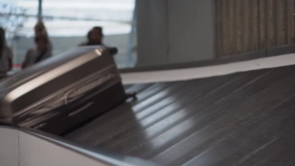 Kufr se pohybuje podél dopravníkového pásu na letišti. Siluety lidí 4k — Stock video