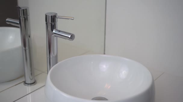White washbasin and chrome tap. Man opens the water in the tap, and closes it