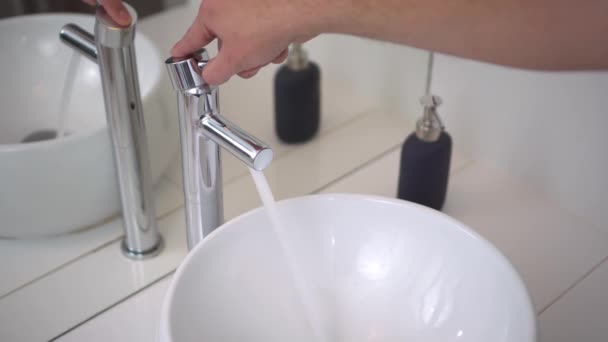 Salle de bains. Évier et robinet en gros plan. La main masculine ouvre et ferme l'eau. 4K — Video